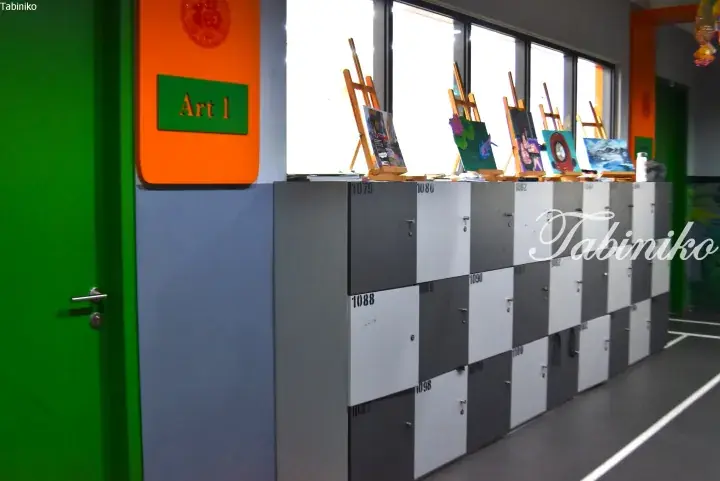 Art 1 classroom lockers with student paintings on easels in a school hallway.