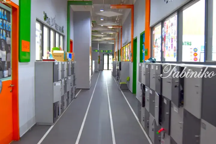 Modern school hallway with grey lockers, white floor lines, and colorful green and orange accents.
