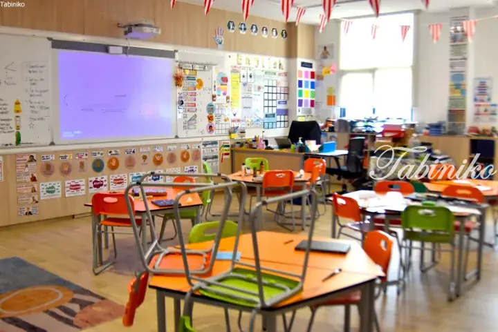 Bright classroom with orange and green chairs, whiteboard, and educational posters.