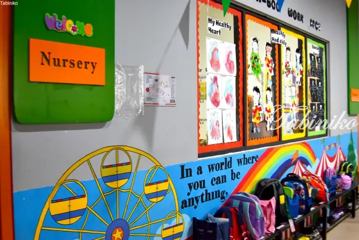 Colorful nursery entrance with a welcome sign, children’s artwork displays, and a motivational quote above a backpack storage area.