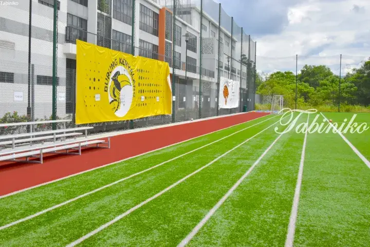 School sports field with green turf, red track, and yellow banner reading Burung Kenyalang.