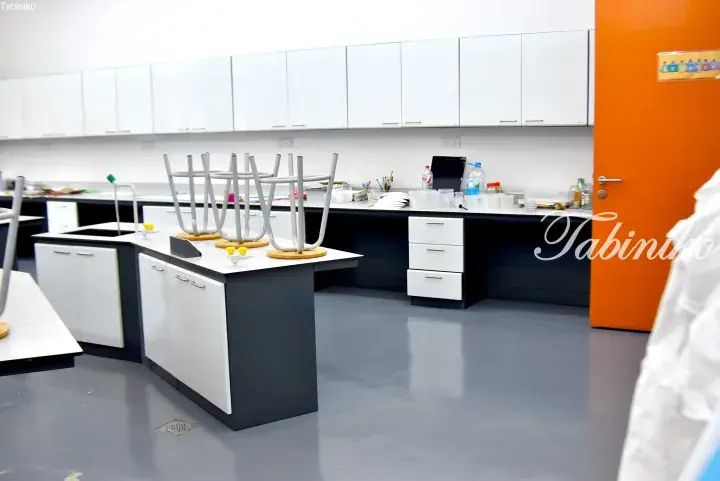 Modern science laboratory with white cabinets, black countertops, and chairs stacked upside down on the work surface.