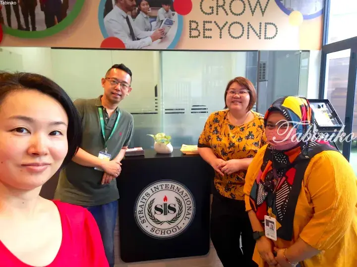 Four people posing at the reception desk of Straits International School with a ‘GROW BEYOND’ banner above.