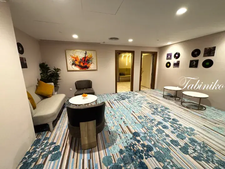 Modern hotel lounge with patterned carpet, seating area, and vinyl record wall decor.