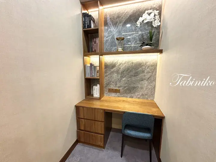 Modern home office corner with wooden desk, built-in shelving, marble accent wall, and blue chair.