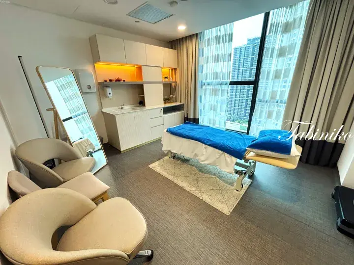 Modern treatment room with massage bed, city view, and beige lounge chairs