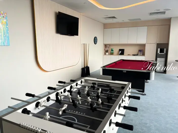 Modern recreational room featuring a foosball table in the foreground and a pool table with red felt in the background.