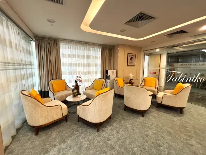 Bright lounge area with cream armchairs and yellow cushions, large windows, and modern lighting.