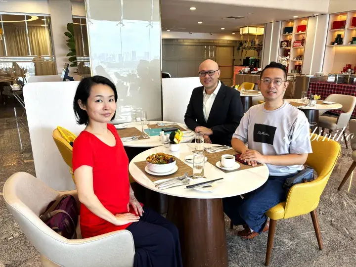 Three people dining at a modern restaurant table with city views in the background.