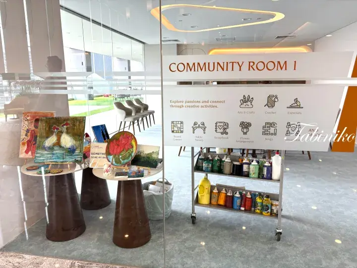 Community Room 1 entrance with art supplies, paintings, and activity icons displayed on a glass wall.