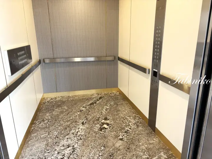 Modern elevator interior featuring marble flooring, cream walls, and stainless steel handrails.