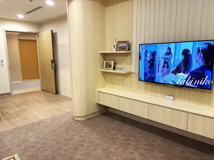 Modern living room with light wood paneling, wall-mounted TV, and floating shelves in a stylish Malaysian home.
