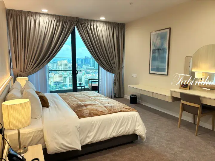 Modern hotel room with a large bed, city view window, and vanity desk in Kuala Lumpur.