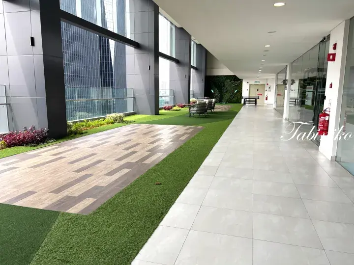 Modern building corridor with artificial grass, wooden decking, and seating area overlooking city skyscrapers.