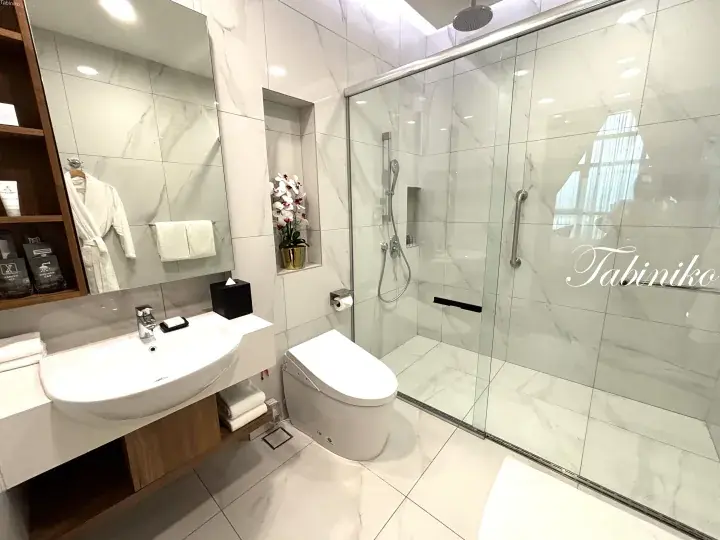 Modern bathroom with marble tiles, glass shower, and wooden vanity in a Malaysian hotel room.