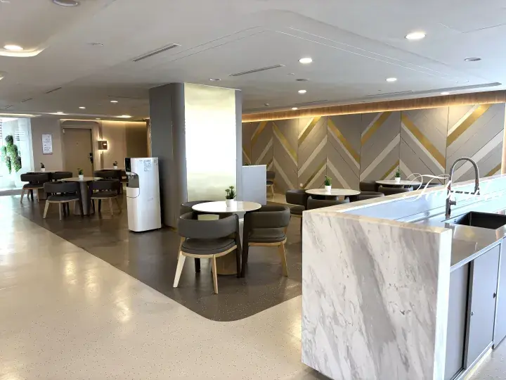 Modern communal kitchen and dining area with marble countertops, grey chairs, and geometric wall panels.
