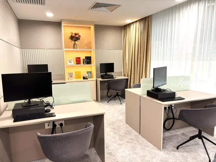 Modern co-working space with three desks, computers, and a decorative shelf in a well-lit room.