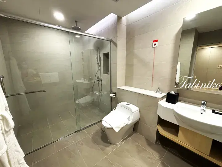 Modern hotel bathroom with glass shower, smart toilet, and wooden vanity in neutral tones.