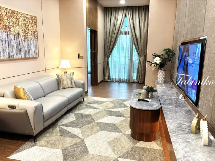 Modern living room with grey leather sofa, geometric rug, marble TV console, and large window with curtains.