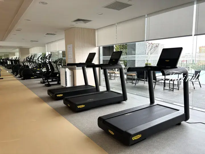 Modern gym with Technogym treadmills and cardio equipment overlooking a city view through large windows.