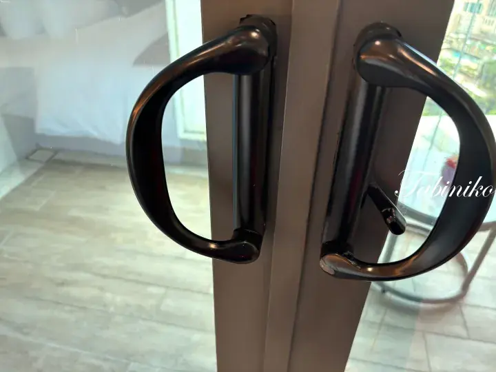 Close-up of modern black metal handles on a glass door leading to a balcony with a city view.