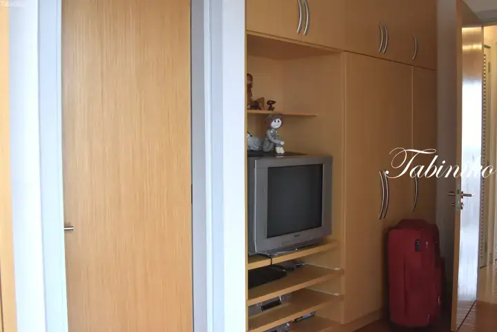 Built-in wooden cabinet housing a CRT television and DVD player, with a red suitcase nearby in a Malaysian apartment.