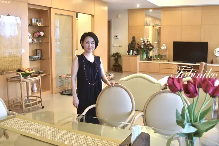 Woman in a black dress standing in a modern dining area with light wood cabinetry and a glass table.