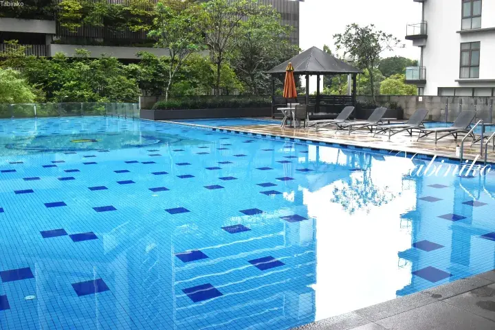 Outdoor swimming pool with blue mosaic tiles, sun loungers, and a gazebo surrounded by lush greenery at a modern property.