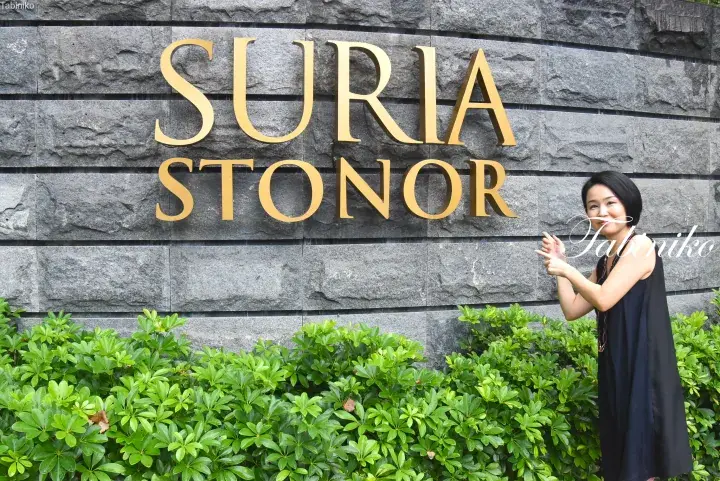 A woman poses in front of the golden Suria Stonor sign on a stone wall.