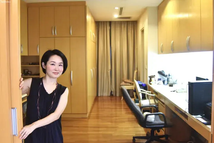 A woman stands smiling in a modern apartment hallway featuring floor-to-ceiling wooden wardrobes and a built-in desk area.