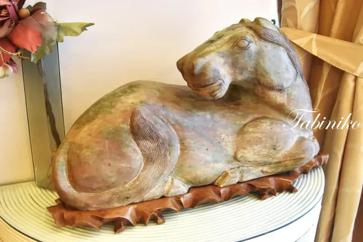 A carved stone sculpture of a resting horse with a natural green and brown finish on a wooden base.