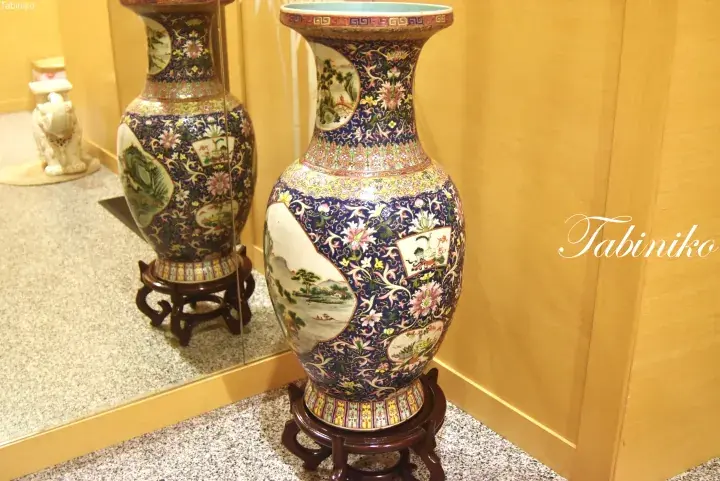 Ornate blue porcelain vase with floral and landscape motifs displayed on a wooden stand.