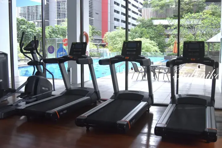 Modern gym with treadmills and elliptical overlooking a swimming pool and lush greenery at a property.