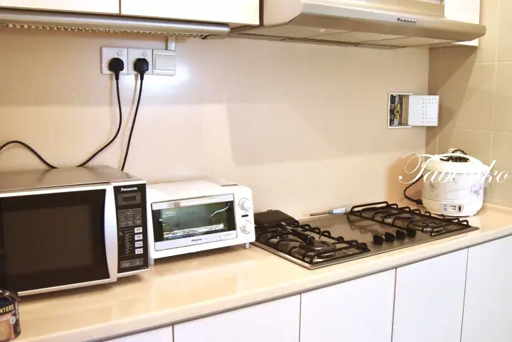 Modern kitchen counter with Panasonic microwave, toaster oven, gas stove, and rice cooker in a Malaysian property.