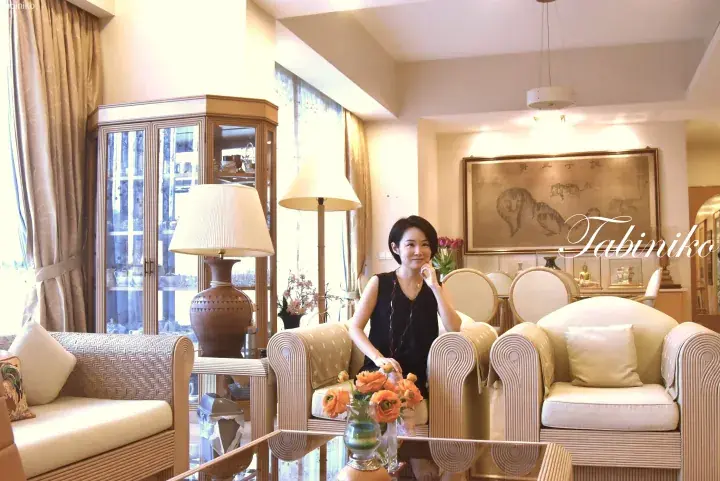 A woman sits in a luxurious living room featuring rattan furniture, a glass display cabinet, and a tiger painting.