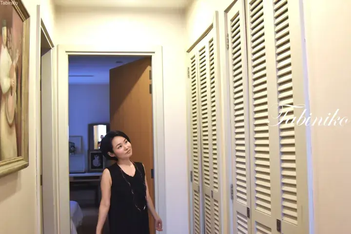 Woman in black dress standing in a hallway with white louvered closet doors and a framed painting.