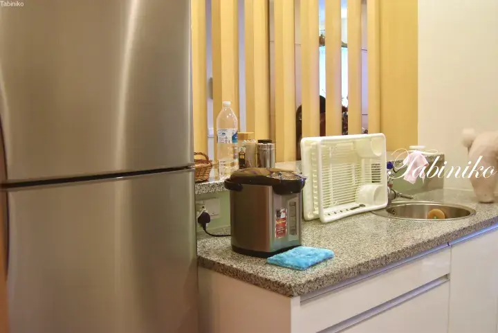 Modern kitchen counter with a stainless steel refrigerator, electric kettle, and dish rack in a Malaysian property.