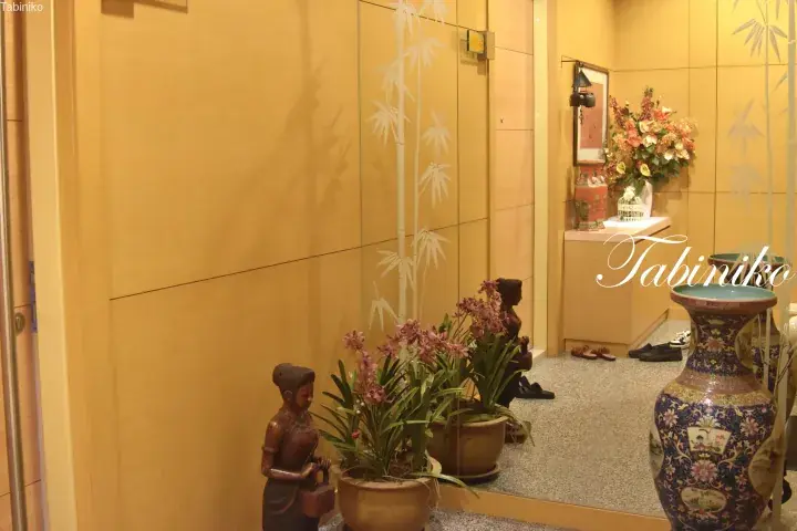 Warm-toned hallway with bamboo wall art, wooden statues, potted orchids, and a large decorative vase.