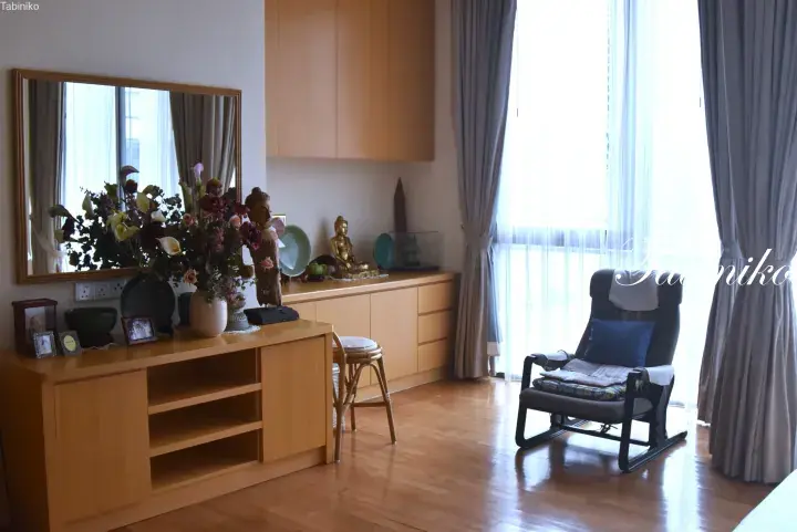 Bright living room with wooden furniture, a massage chair, and a display of Buddha statues and flowers near a window.