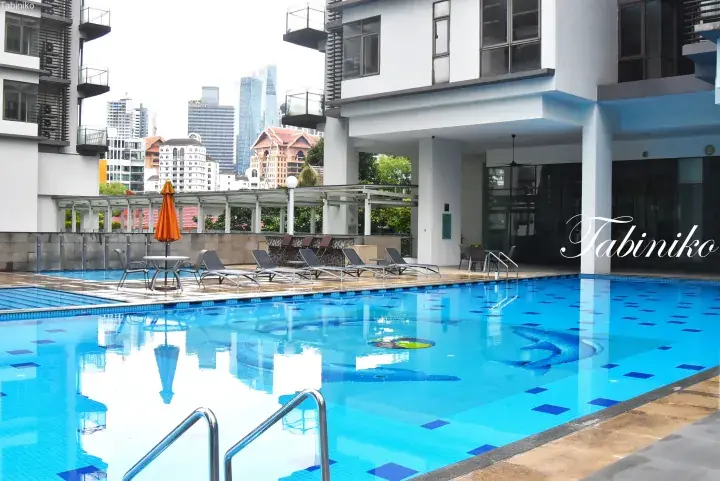 Swimming pool with blue mosaic tiles and lounge chairs at a Kuala Lumpur serviced residence, with city skyline in background.