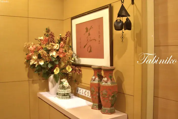 Warmly lit interior corner with floral arrangement, calligraphy art, and decorative vases in a Malaysian property.