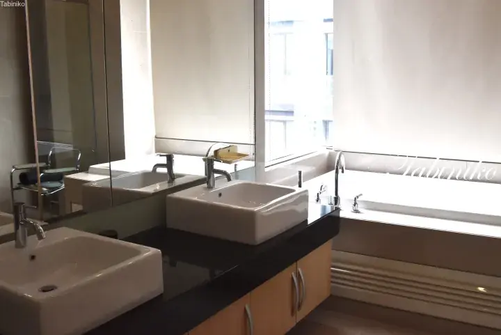 Modern bathroom with dual white vessel sinks on a black countertop and a large bathtub near a window.
