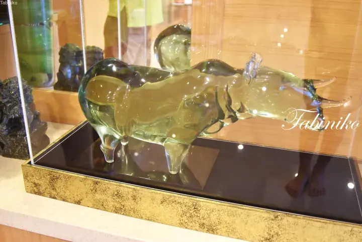 Translucent green glass bull sculpture displayed in a glass case with a gold base.