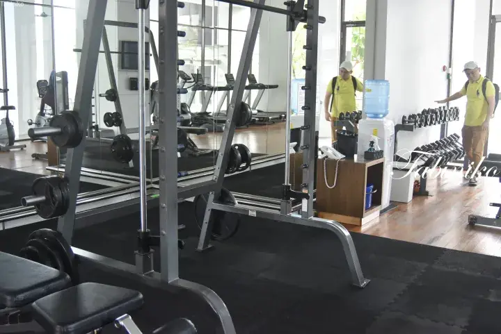 A well-equipped gym featuring a Smith machine, dumbbell rack, and cardio equipment with large windows and mirrors.