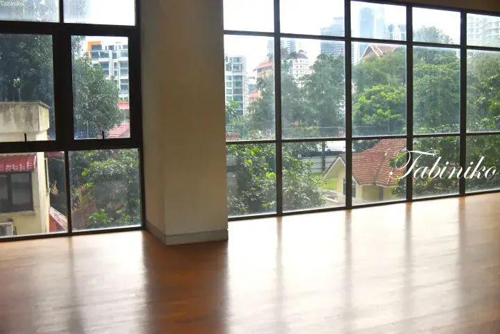 Spacious room with polished wooden floors and large windows overlooking lush greenery and city buildings in Kuala Lumpur.