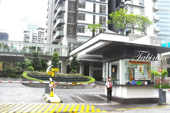 Security guard at the entrance gate of a modern residential building in Malaysia, with visitor and resident lanes.