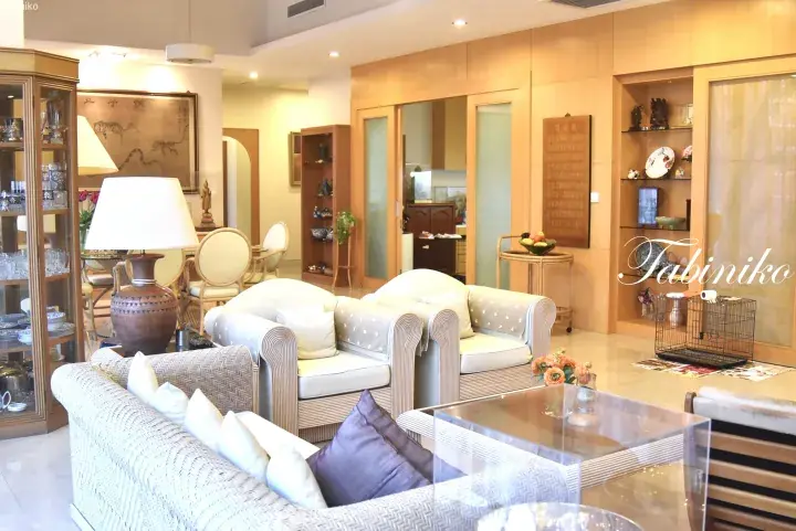 Bright living room with rattan furniture, glass display cabinets, and traditional Asian artwork.