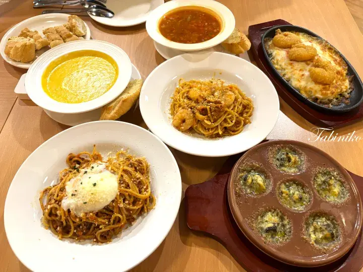 Spread of Italian dishes including spaghetti, soup, and escargot on a wooden table.