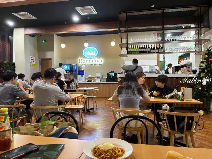 Romaliya casual Italian restaurant interior with wooden tables, wine shelves, and diners enjoying pasta.