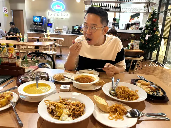 Man eating spaghetti at Romaliya Italian restaurant in Malaysia, with various pasta dishes and soup on the table.